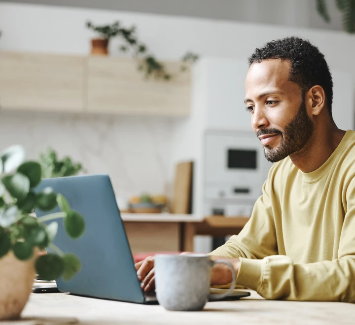 Male on laptop sitting at a table in the kitchen of a home. 