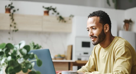 Male on laptop sitting at a table in the kitchen of a home. 