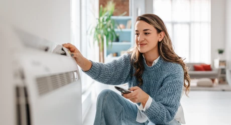 Woman knelt to adjust air conditioning unit in interior of home.   
