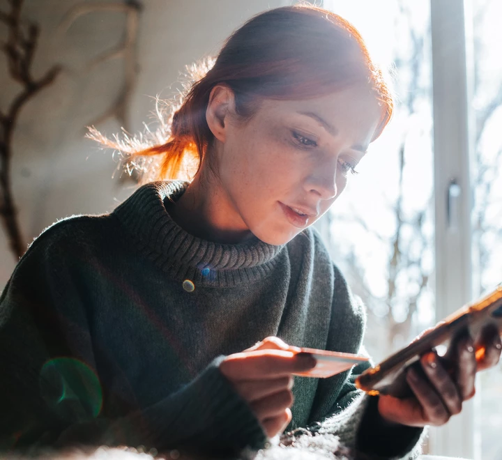 Young woman shopping online with phone and credit card. Woman is looking at the phone; credit card is in her hand. 