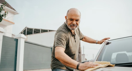 Senior man outside in driveway washing his car. 