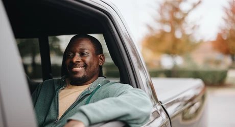 African American man smiling while driving a pickup truck in autumn. 