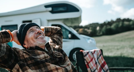 Smiling middle aged man camping and relaxing with his hands behind his head 