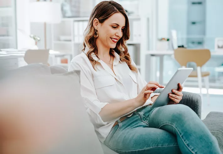 Woman seated on sofa in brightly lit office looking at tablet 