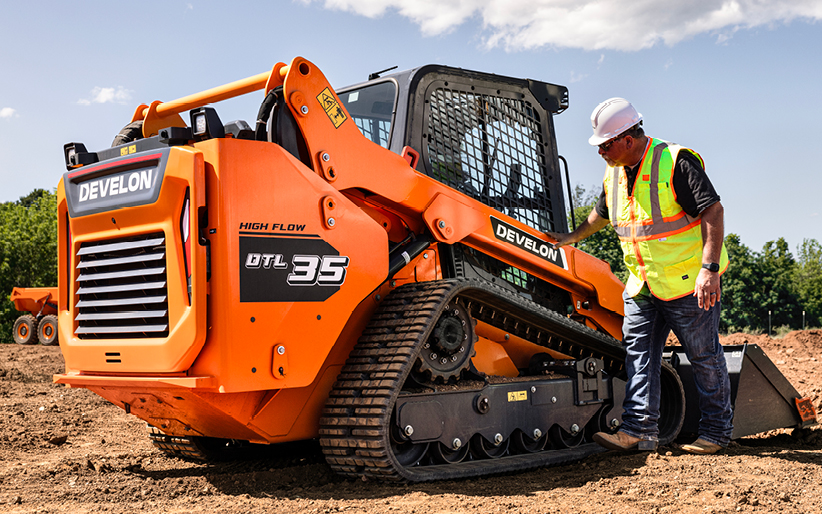 An operator carefully inspects a compact track loader to identify wear and tear before it leads to downtime.