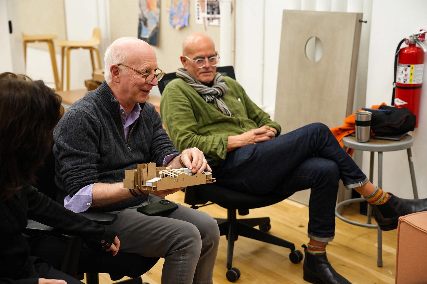 Professor Paul Goldberger, holding a student-created 3D Blockology model, sits beside Professor Alfred Zollinger as they engage with students during a discussion of final projects.