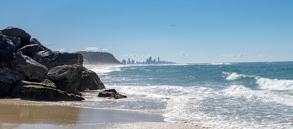 Ocean waves coming up to the rocks at Palm Beach, with the Gold Coast skyline in the background
