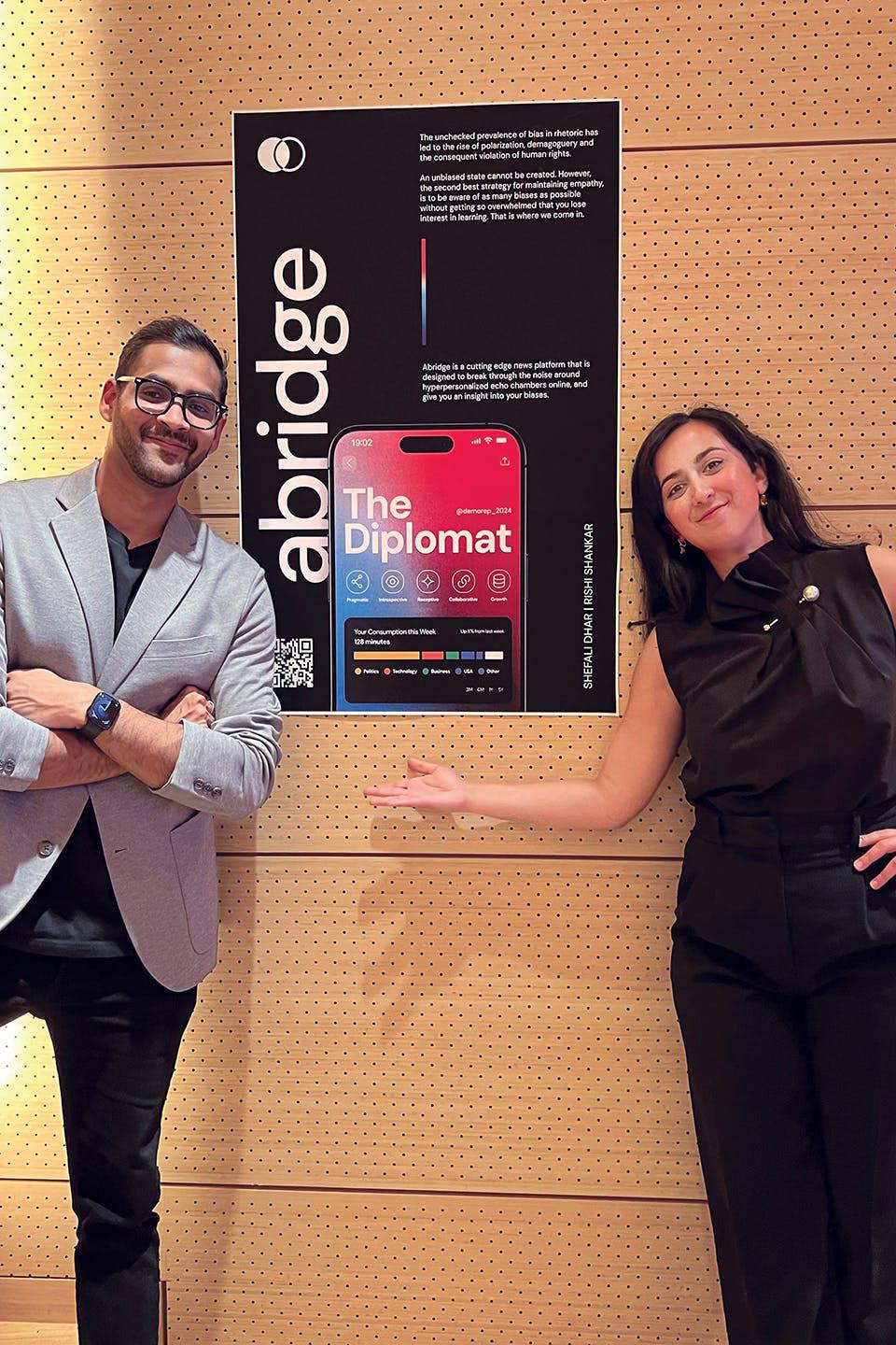 Shankar and Dhar pose in front of a poster of their app.