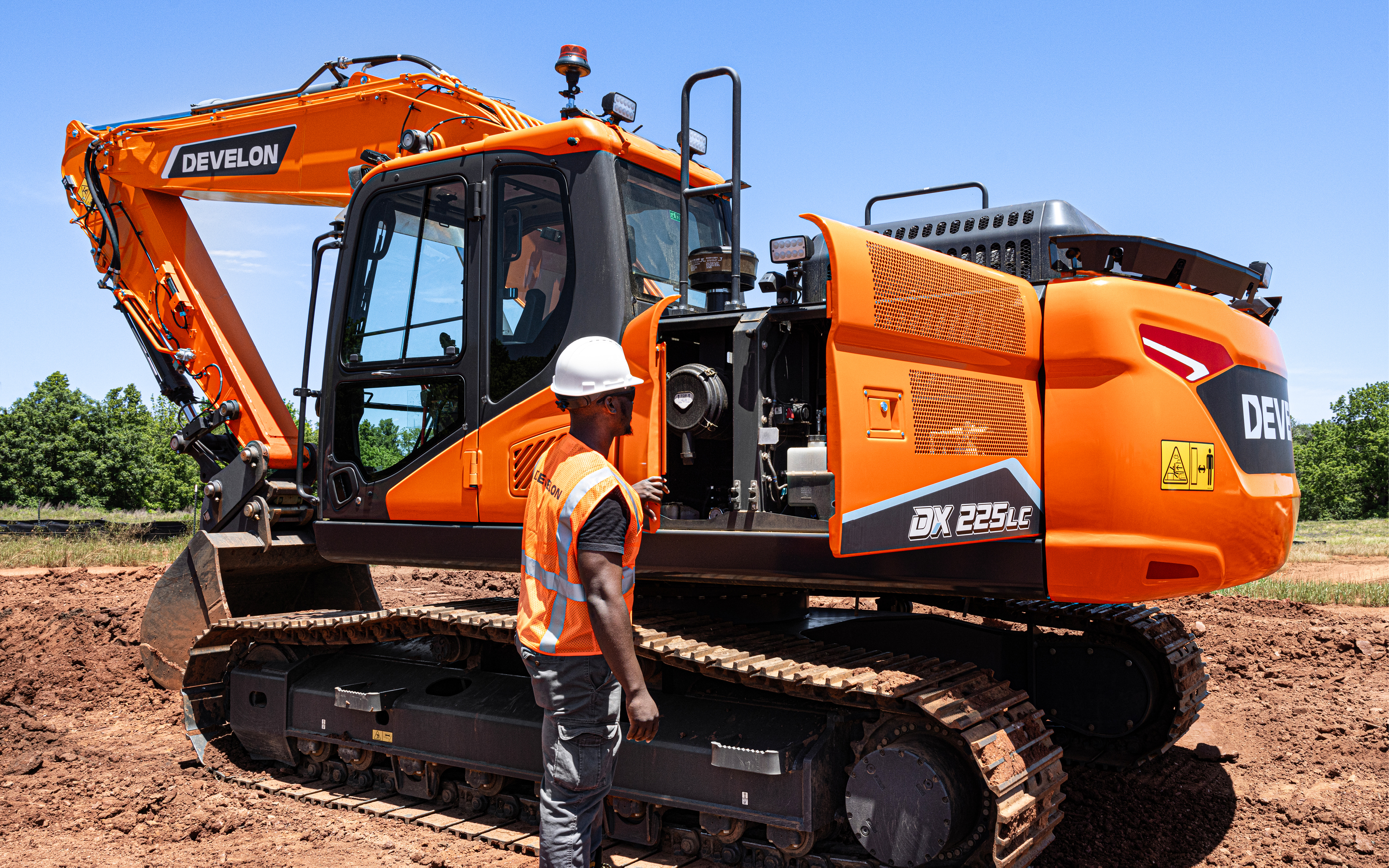 An operator inspecting the internal components of a DEVELON DX225LC-7 crawler excavator.