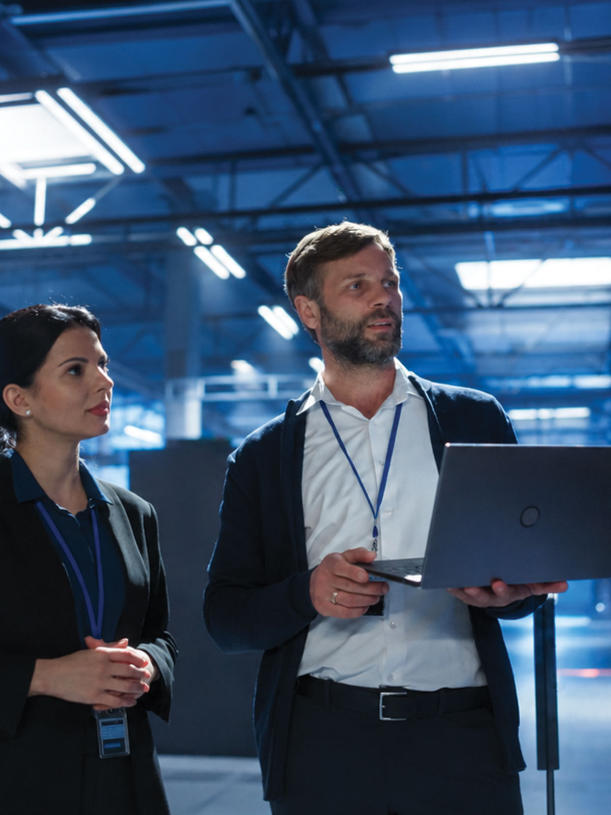 Two ICT professionals wearing ID lanyards holding a laptop while analyzing data center operations