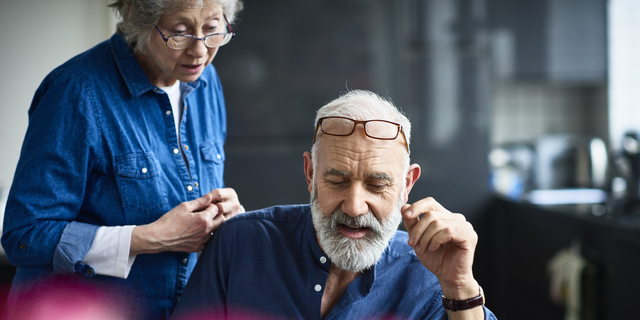 Hipster senior man with beard using laptop and woman watching