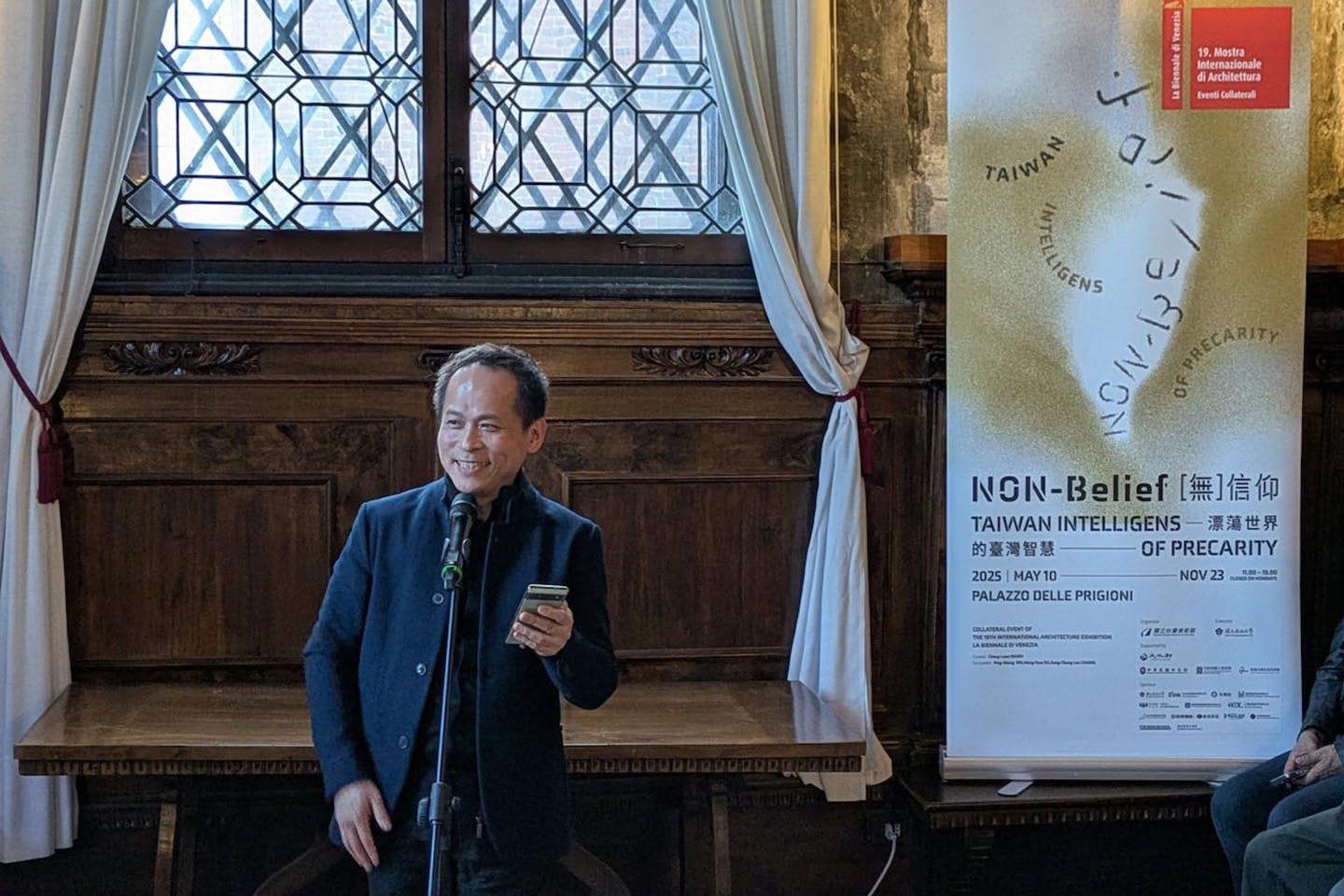 Professor Cheng-Luen Hsueh speaks into a microphone while standing at the 2025 Venice Biennale of Architecture.