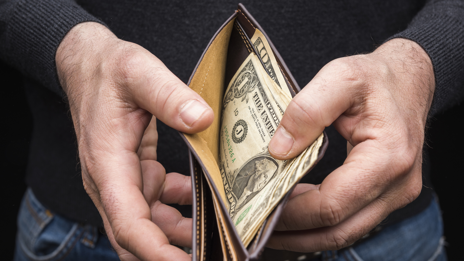 Hands holding a wallet with a small amount of US dollars, close up