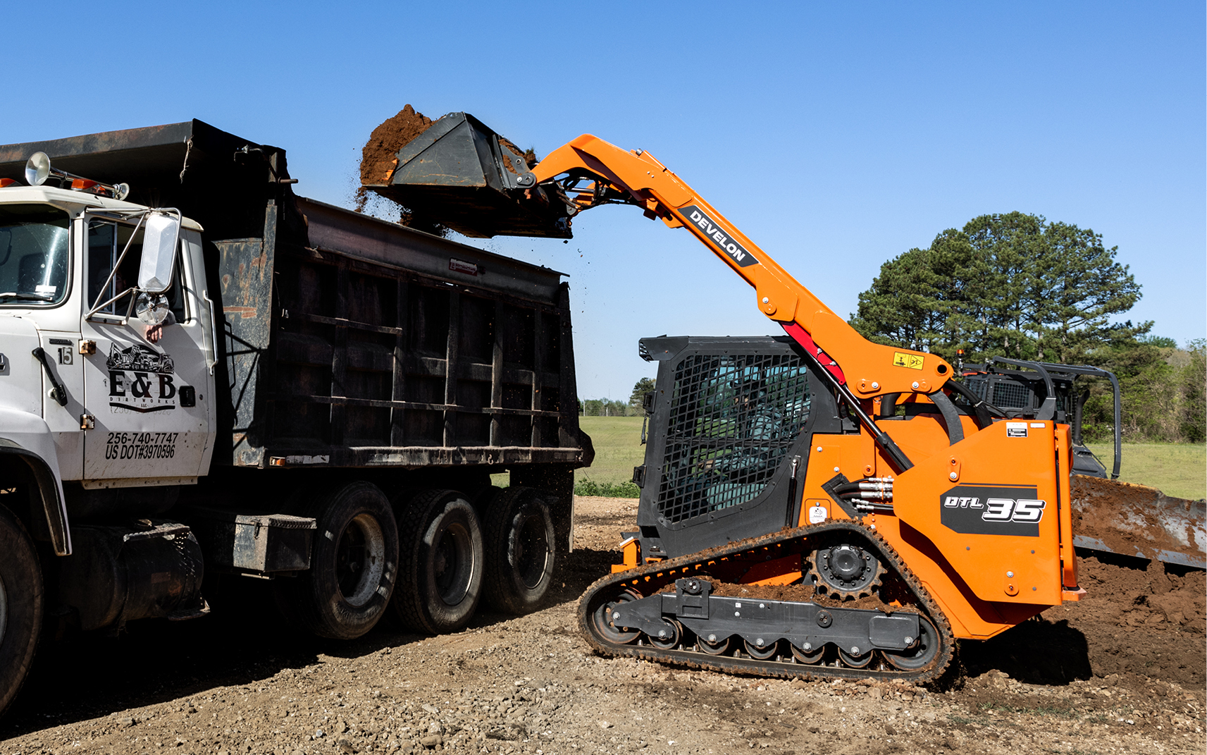 DEVELON DTL35 compact track loader dumping dirt into a high-sided dump truck.