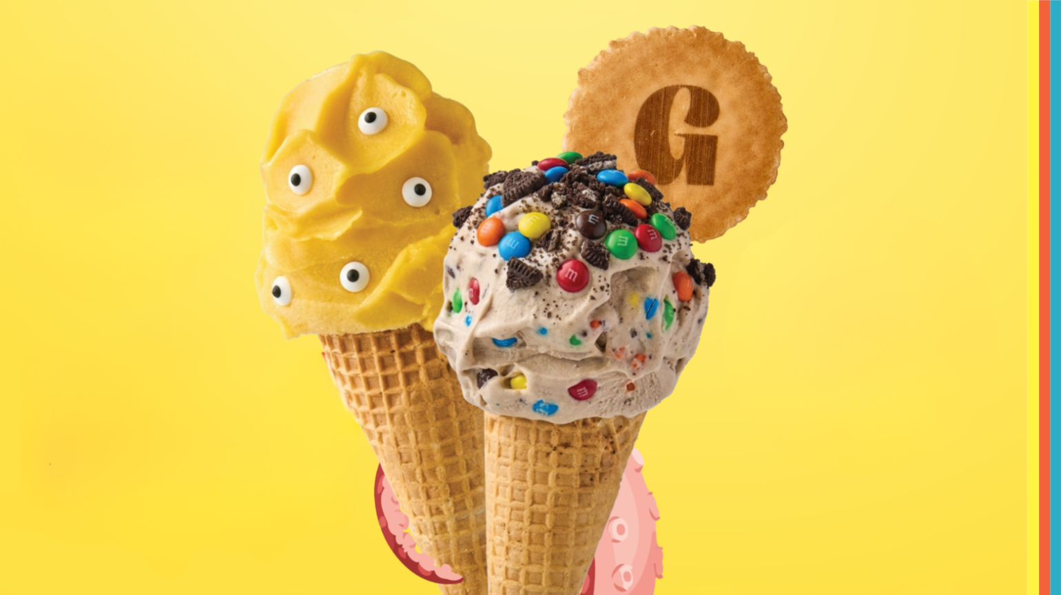 Two colourful Gelatissimo gelato cones against a bright yellow background, featuring playful monster-inspired creations. One cone is topped with yellow gelato decorated with candy eyeballs, while the other features cookies-and-cream gelato covered in chocolate cookie crumbs, colourful chocolate candies and a branded biscuit.