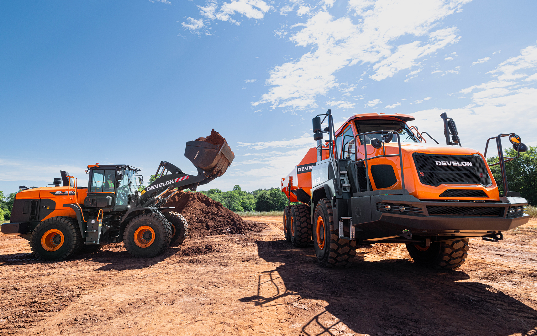 A DEVELON wheel loader preparing to dump dirt into the bed of a DEVELON articulated dump truck.