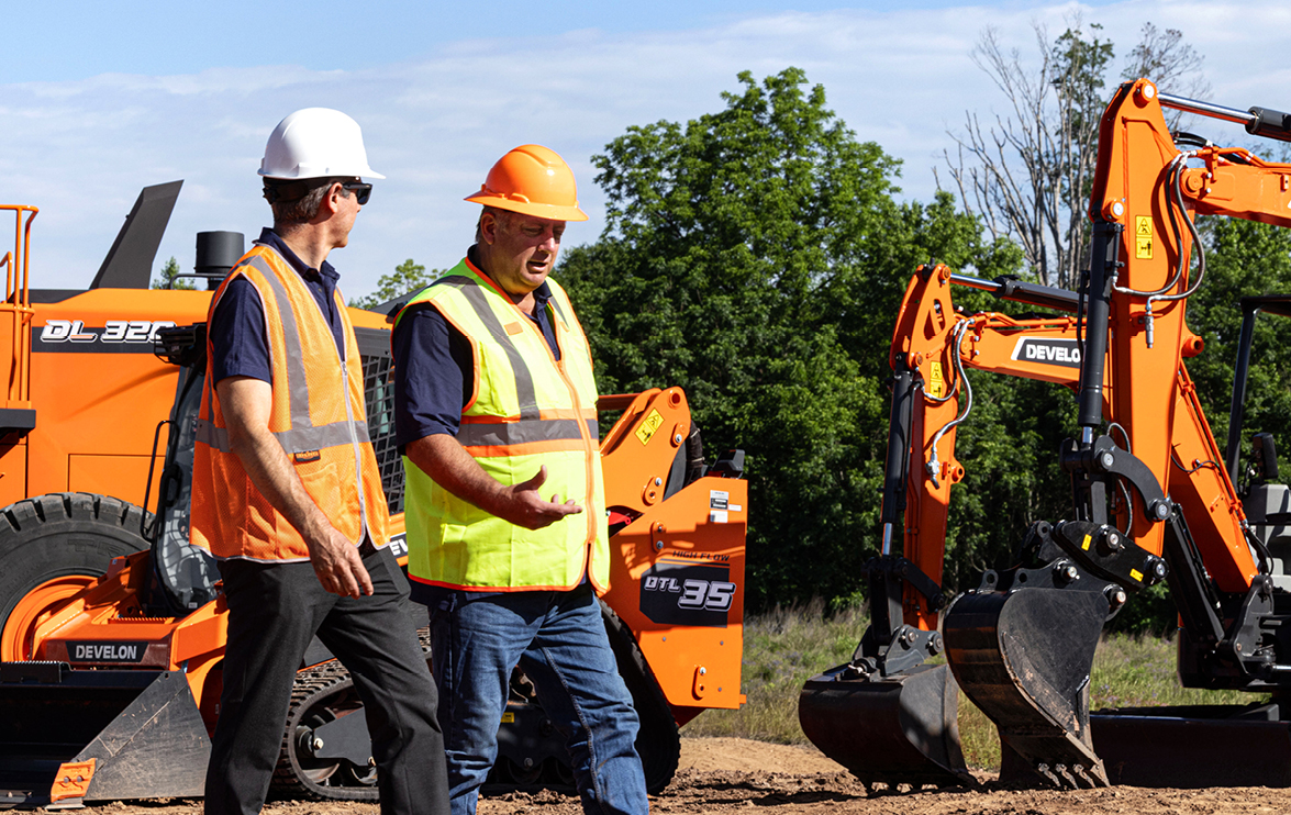 A DEVELON dealer talks with a customer in front of a lineup of DEVELON construction equipment.