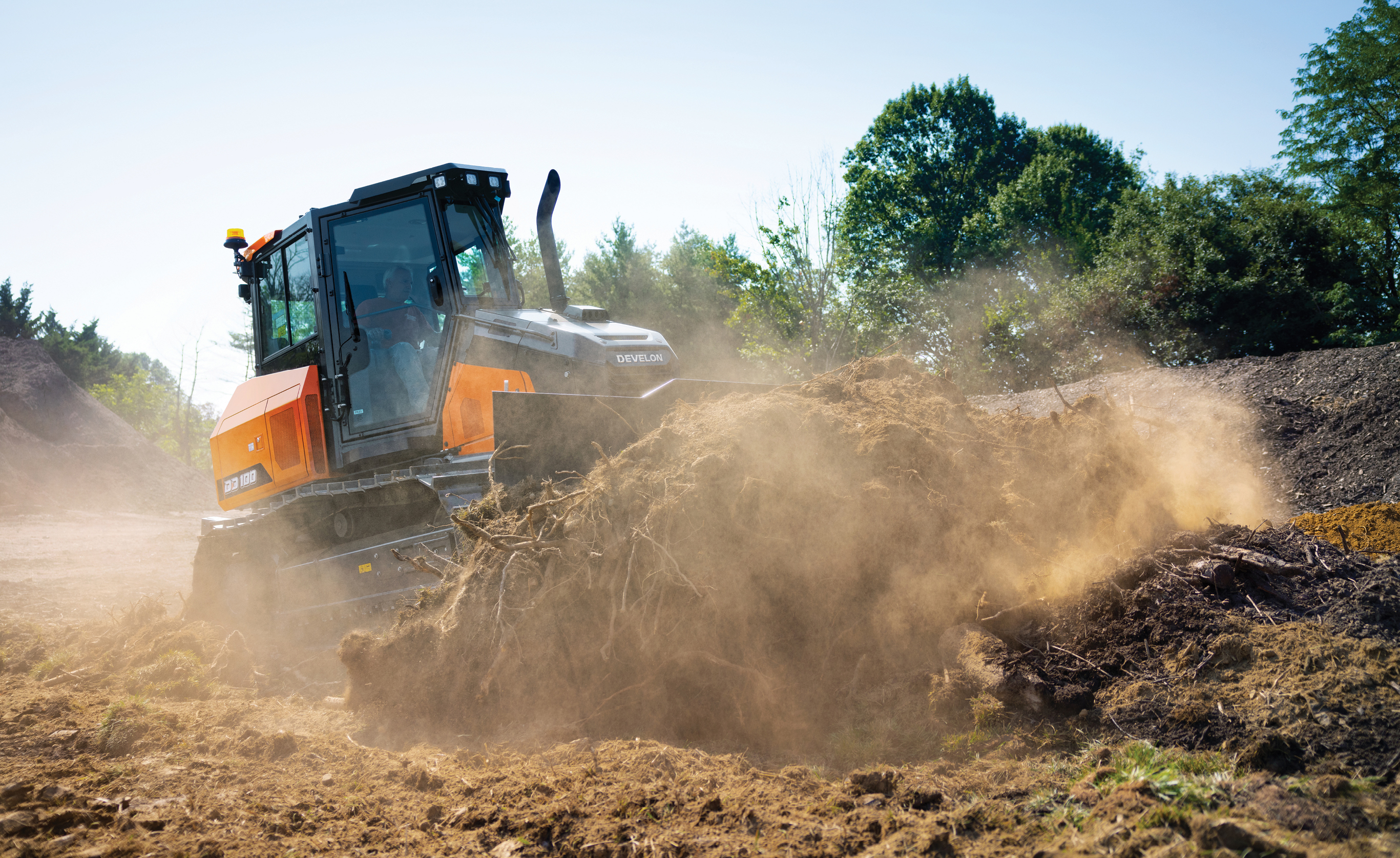 A DEVELON DD100 dozer pushing a pile of dirt on a job site.