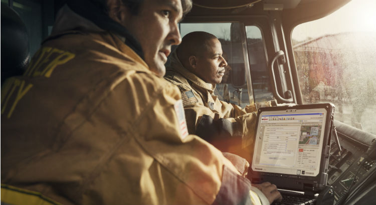 Two fire EMS responders use a toughbook rugged laptop as part of their firefighting gear kit in the field.
