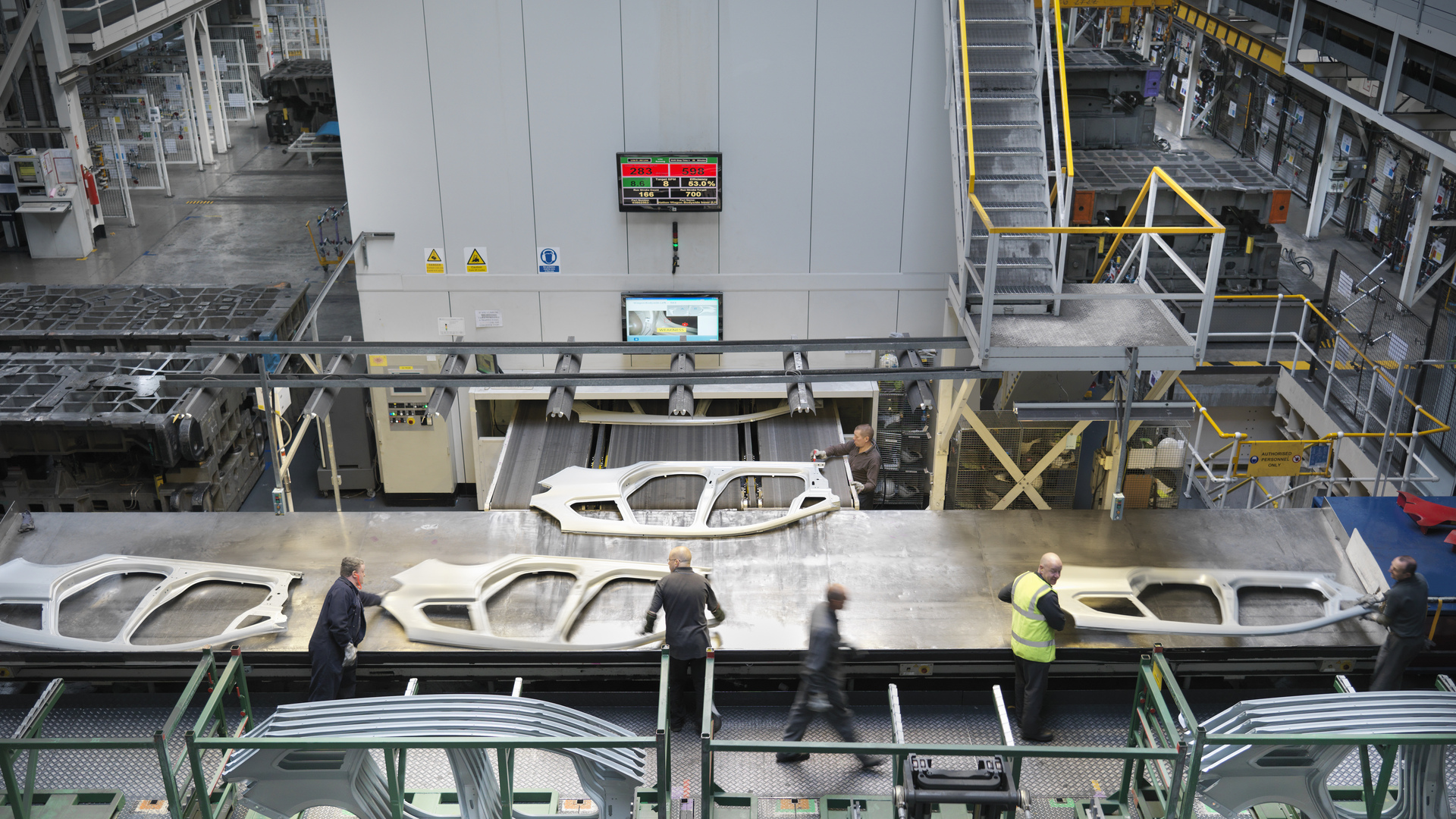 High angle view of workers handling car parts as they come out of press in car factory