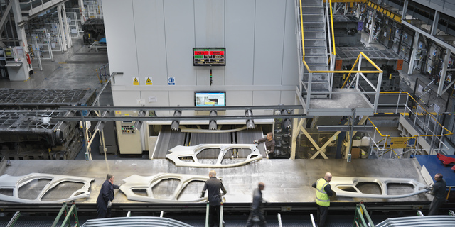 High angle view of workers handling car parts as they come out of press in car factory