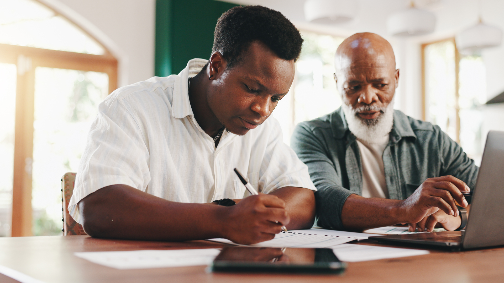 Father, son and laptop in home for finance paperwork, writing or mortgage application with senior. Budget document, men and help with loan contract or teaching investment planning with African family