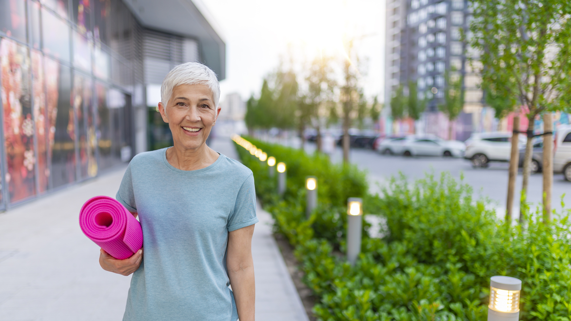 Gorgeous senior woman carrying a yoga mat outdoors and smiling