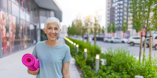 Gorgeous senior woman carrying a yoga mat outdoors and smiling