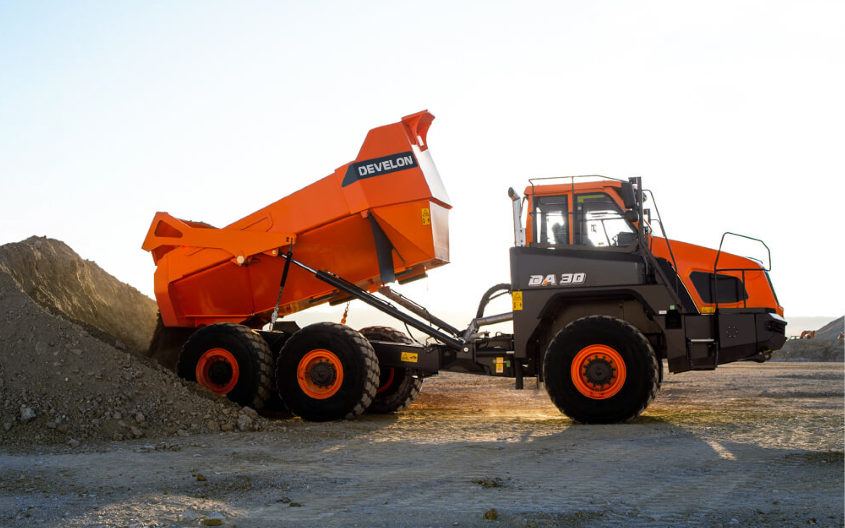 A DEVELON DA30 articulated dump truck raises its dump bed to unload material.