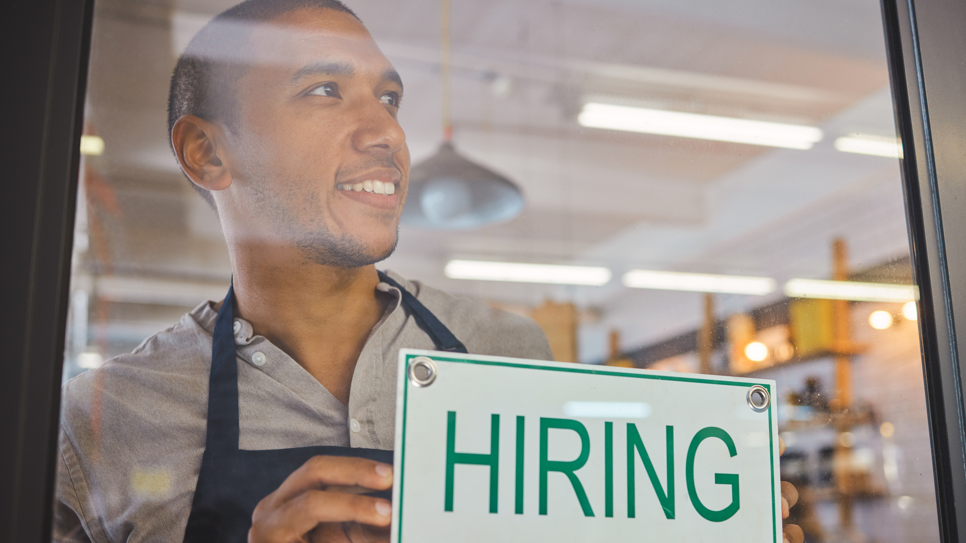 Recruitment, advertising and small business owner with hiring sign board on window or door of cafe or restaurant, happy and positive. Young business man excited open after end of covid virus pandemic