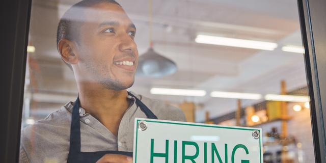 Recruitment, advertising and small business owner with hiring sign board on window or door of cafe or restaurant, happy and positive. Young business man excited open after end of covid virus pandemic