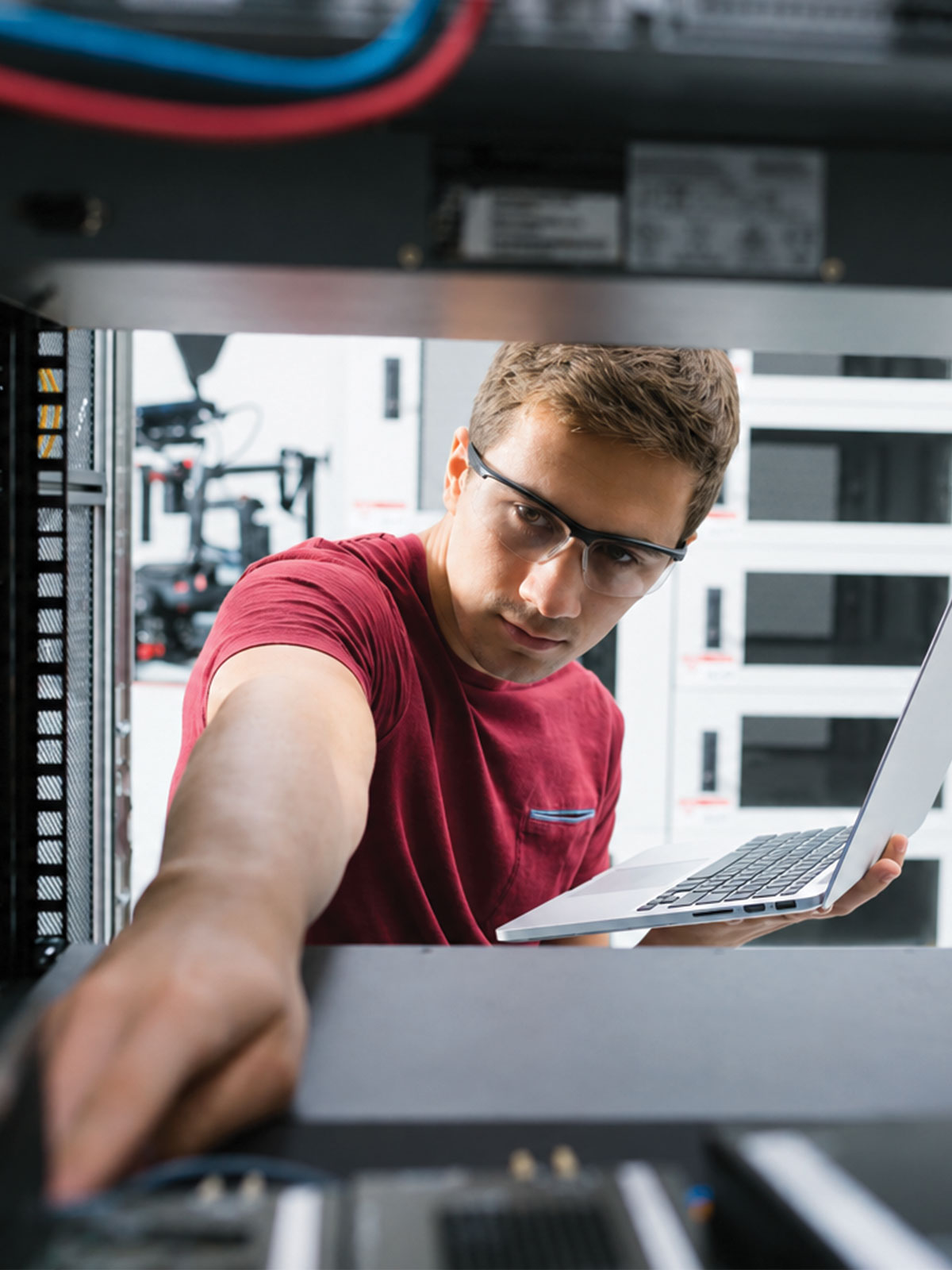 Server technician working inside a data center rack while holding a laptop and wearing safety glasses