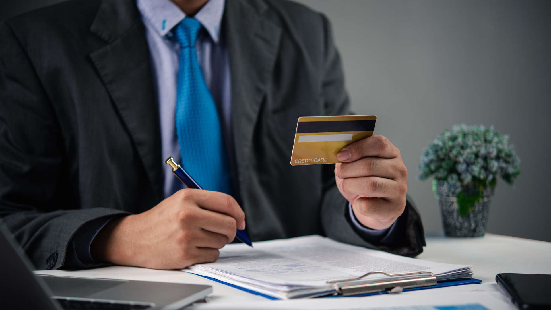 Businessman holding credit card and writing financial report. Online banking, payment management, and budget planning for personal finance analysis, transaction and business use.