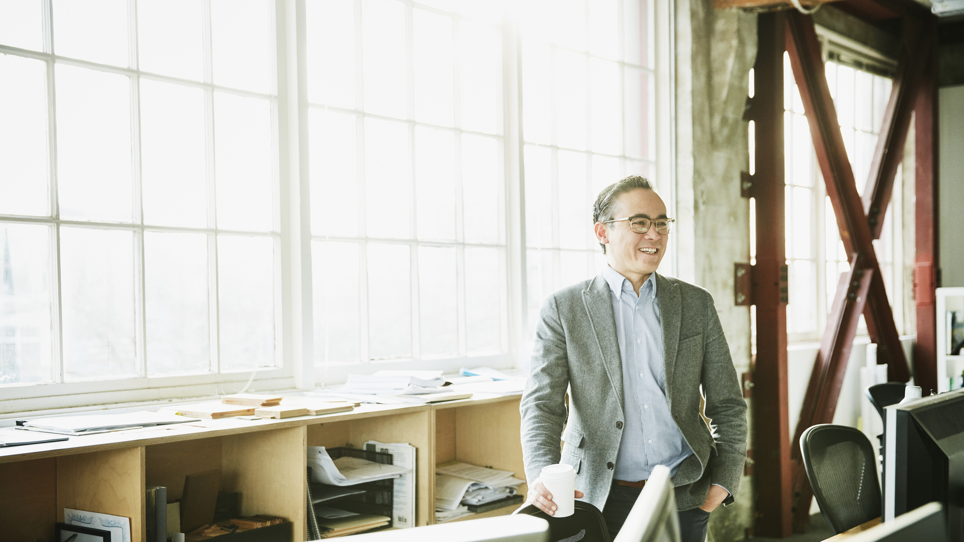 Portrait of smiling businessman standing at office workstation holding coffee cup