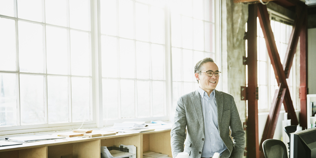 Portrait of smiling businessman standing at office workstation holding coffee cup