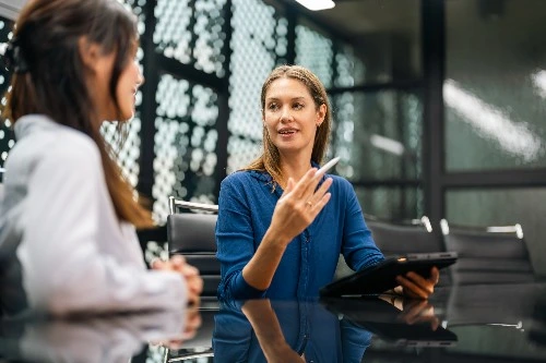 Image of two human resources personnel in the services industry, chatting while one holds on to a tablet