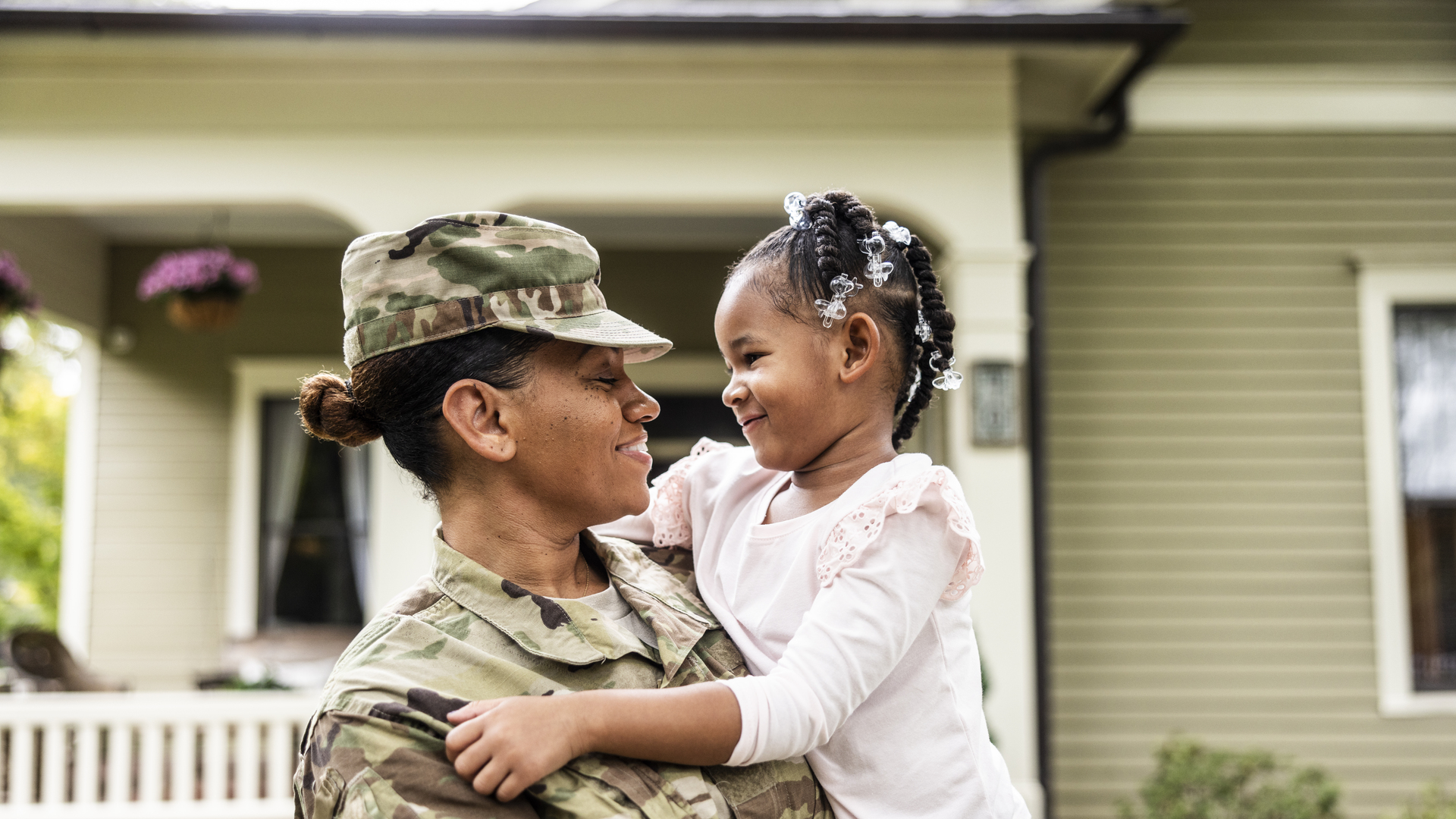 Portrait of female U.S. soldier in uniform with young daughter in front of home