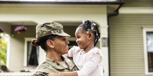 Portrait of female U.S. soldier in uniform with young daughter in front of home