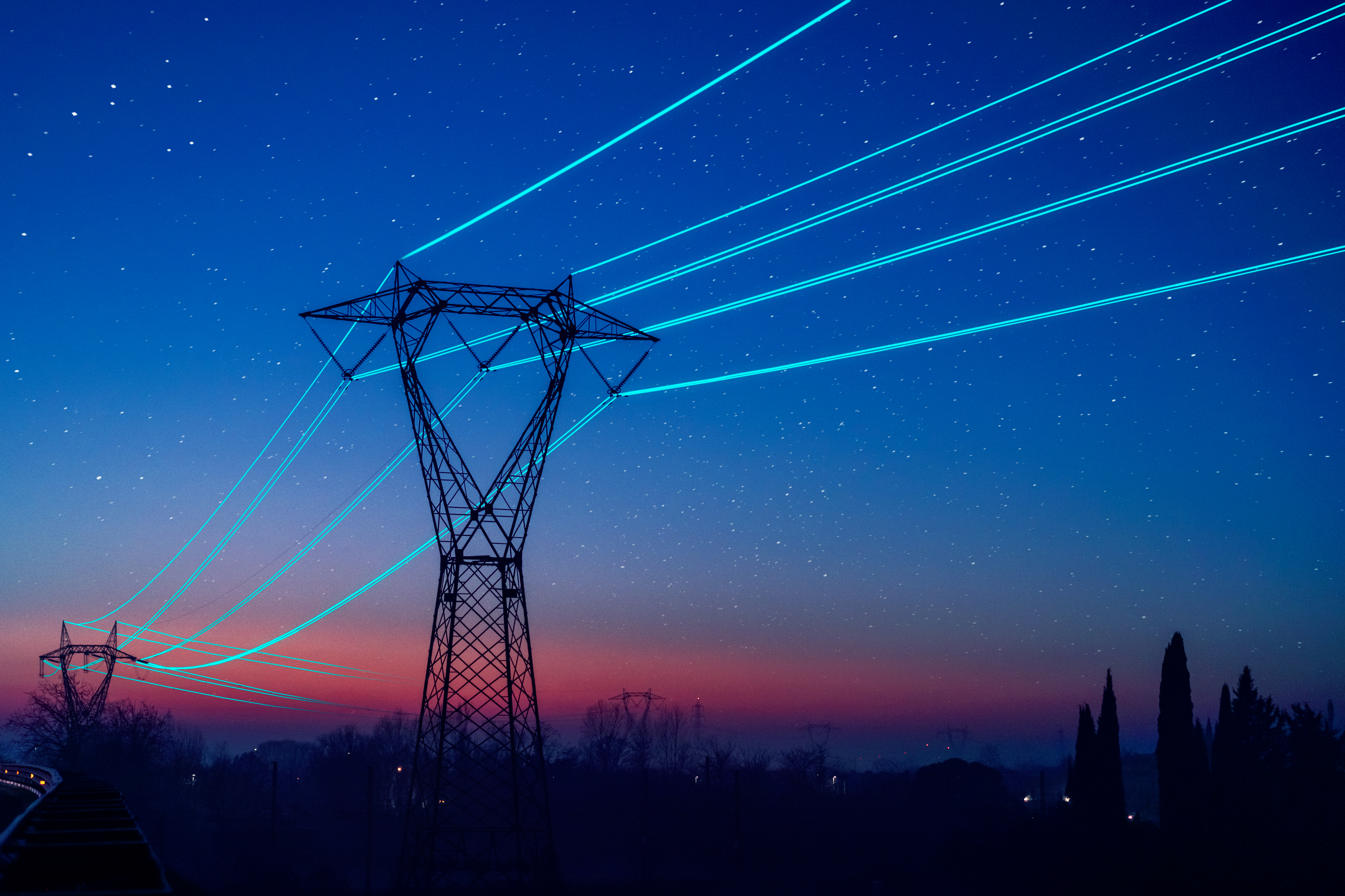A field services electrical tower at sunset with glowing blue power lines.