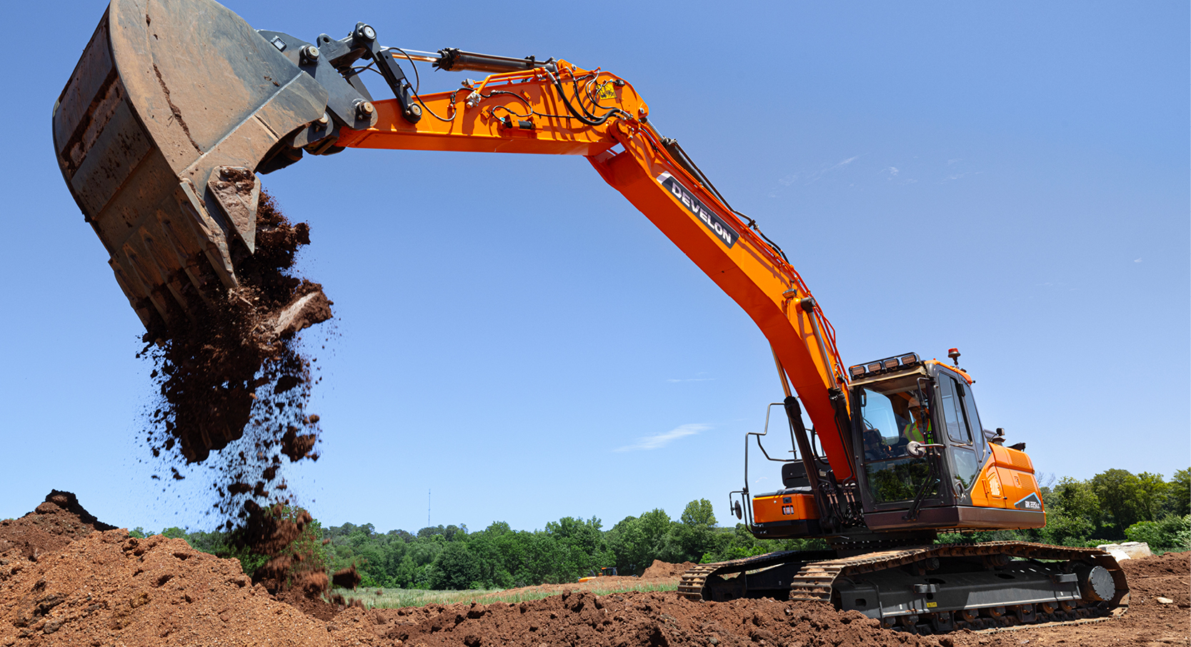 A DEVELON crawler excavator dumps dirt on a job site.