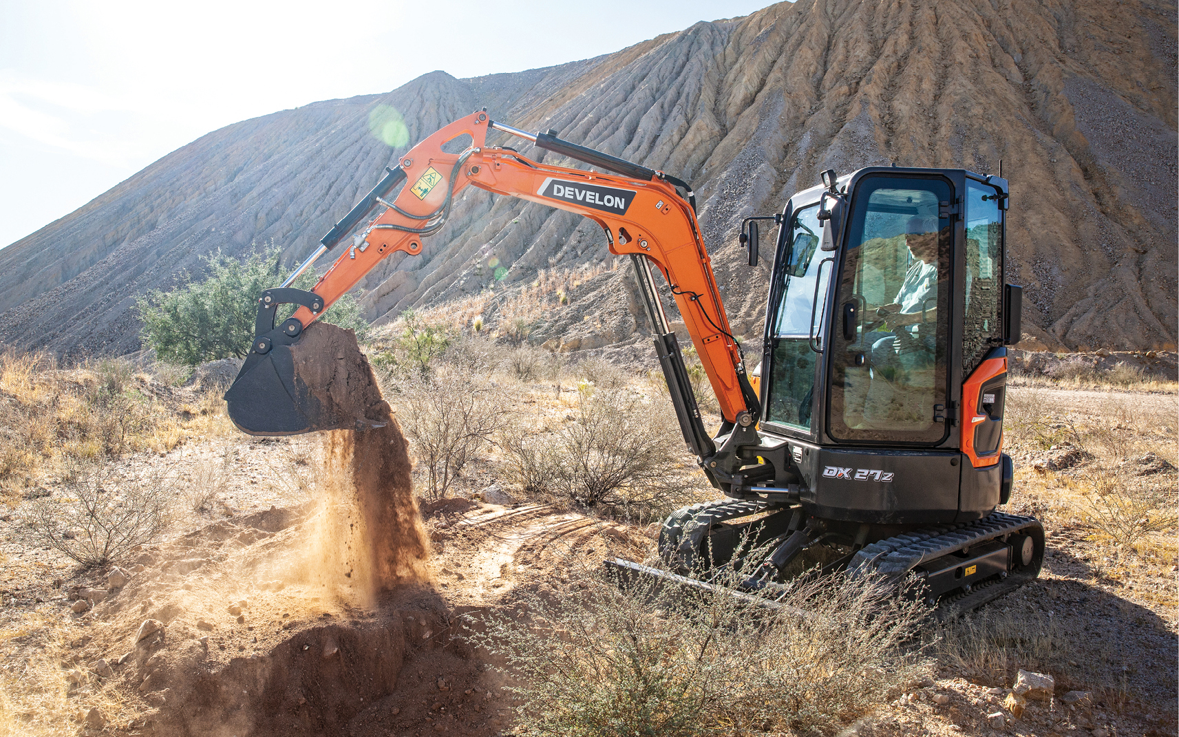 DEVELON mini excavator scoops dirt on a remote work site.