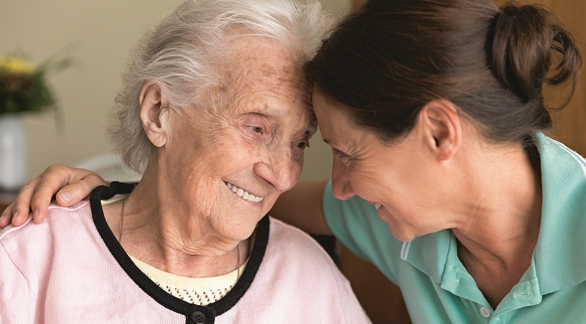 A caregiver and senior adult woman sharing a smile together