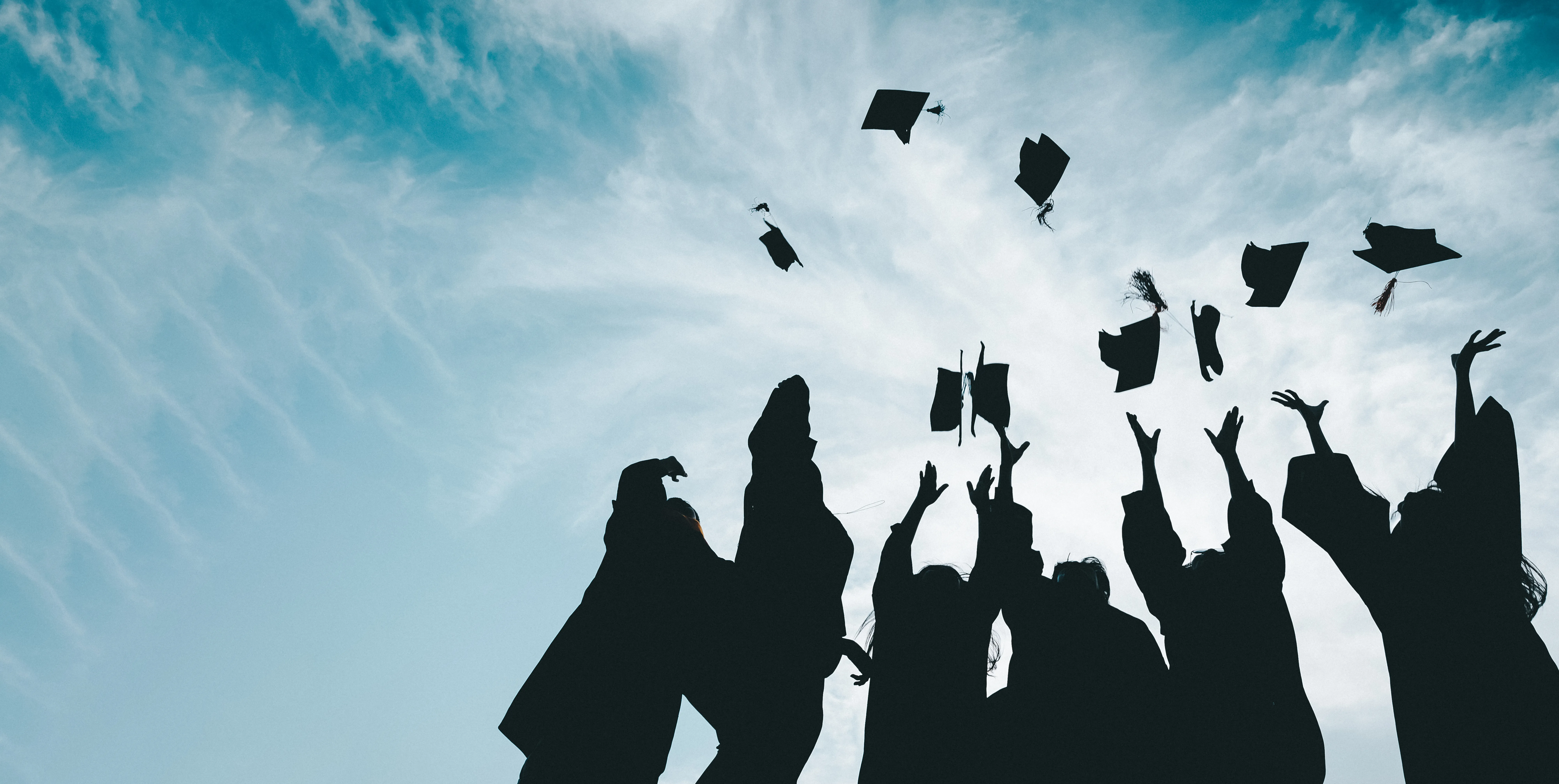 Silhouettes of students celebrating graduation. Blue sky with clouds in the background. 