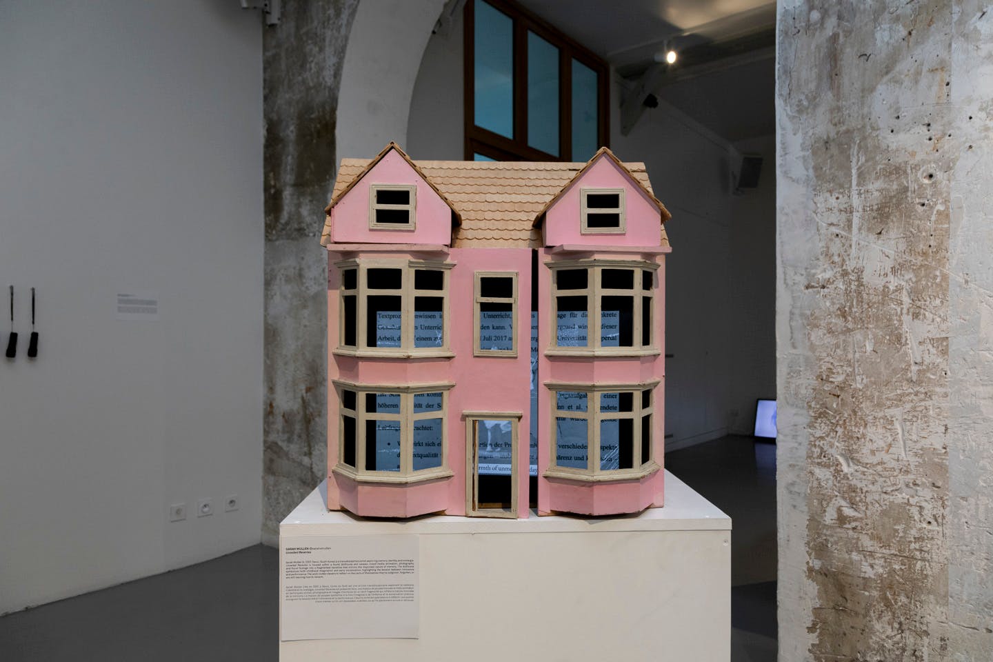 Pink dollhouse model with text panels inside displayed on pedestal