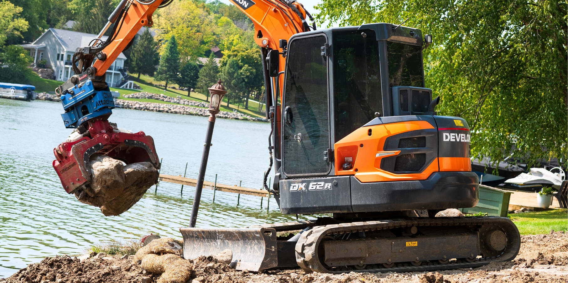 A DEVELON mini excavator lifting landscape boulders on a job site.