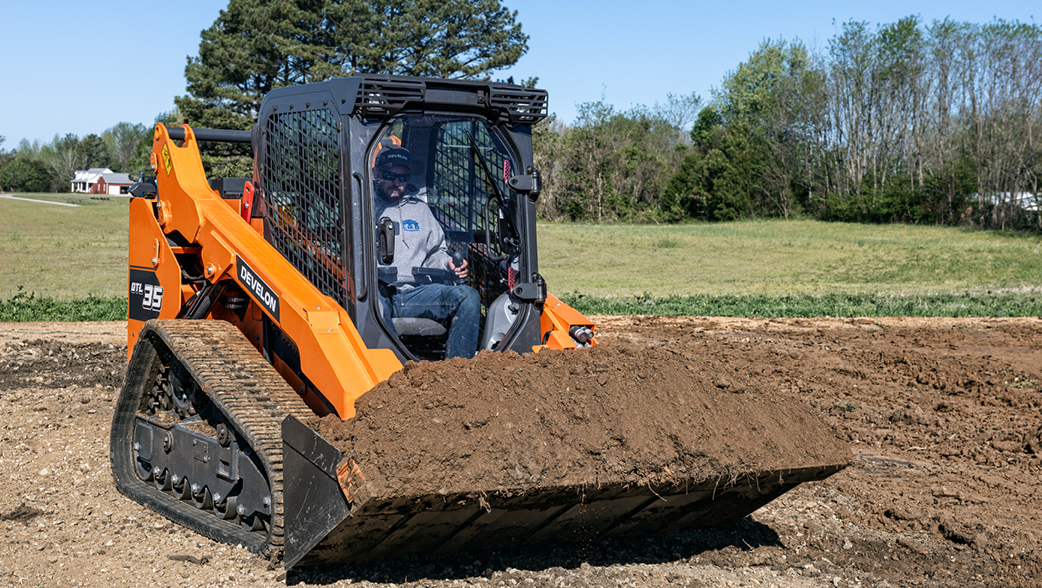 A DEVELON compact track loader hauling a large pile of dirt on a job site.