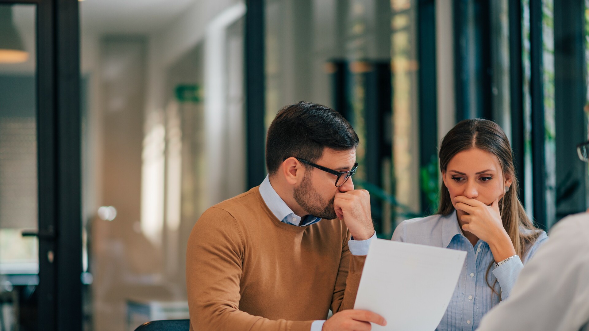 Portrait of a couple with financial problems looking at document in financial adviser's office.