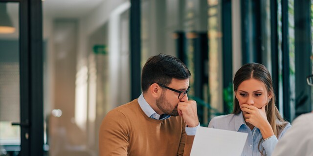 Portrait of a couple with financial problems looking at document in financial adviser's office.