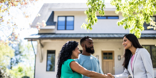 Couple meeting with real estate agent in front of home