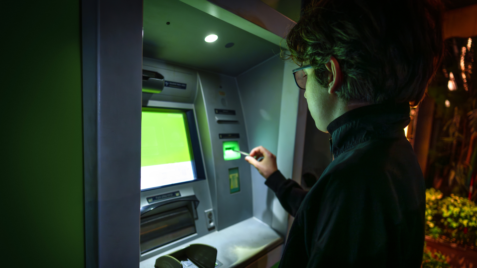 Teenager inserting bank card into ATM machine